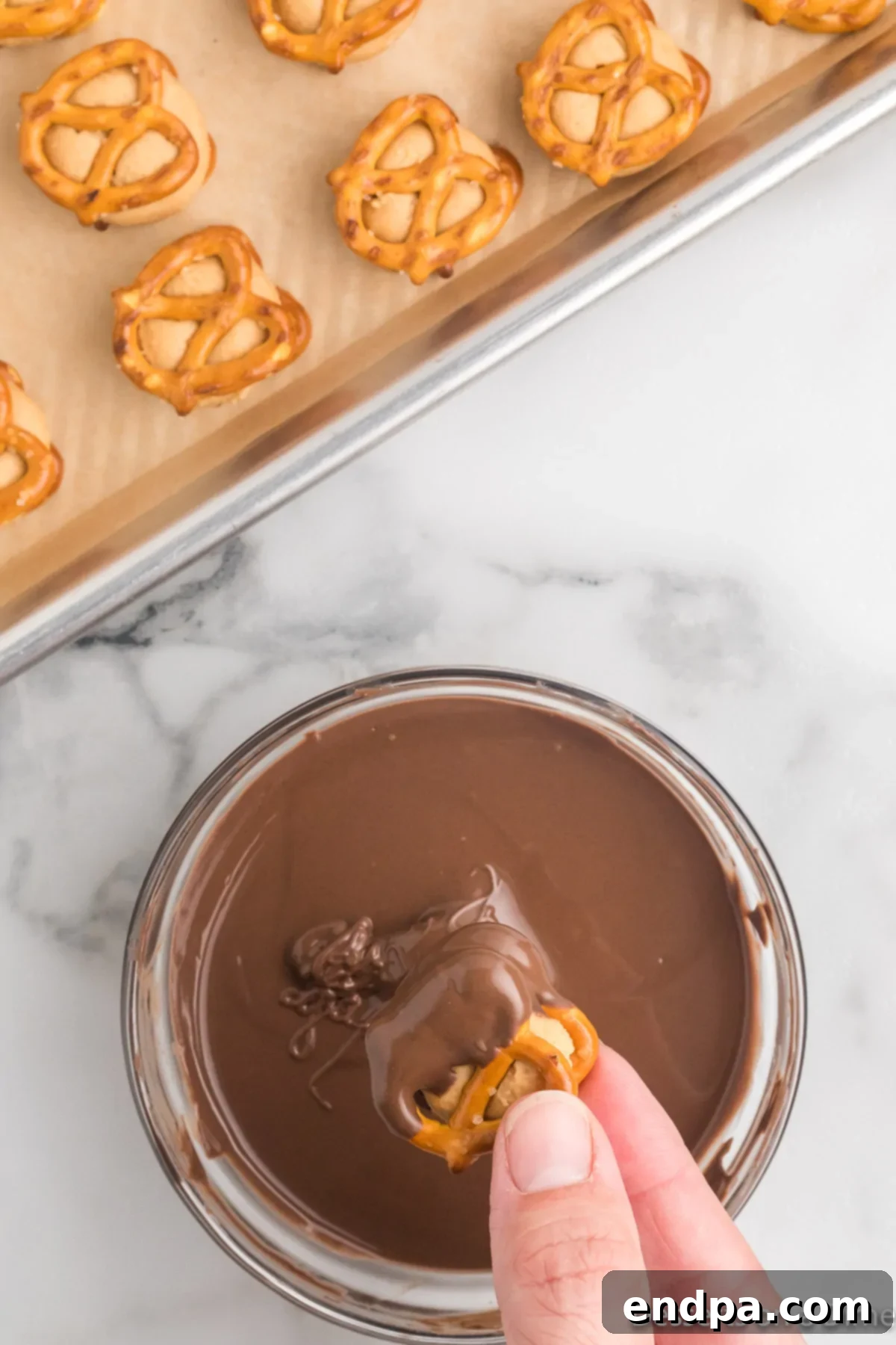 A pretzel bite being carefully dipped halfway into the melted chocolate, with excess chocolate dripping off.