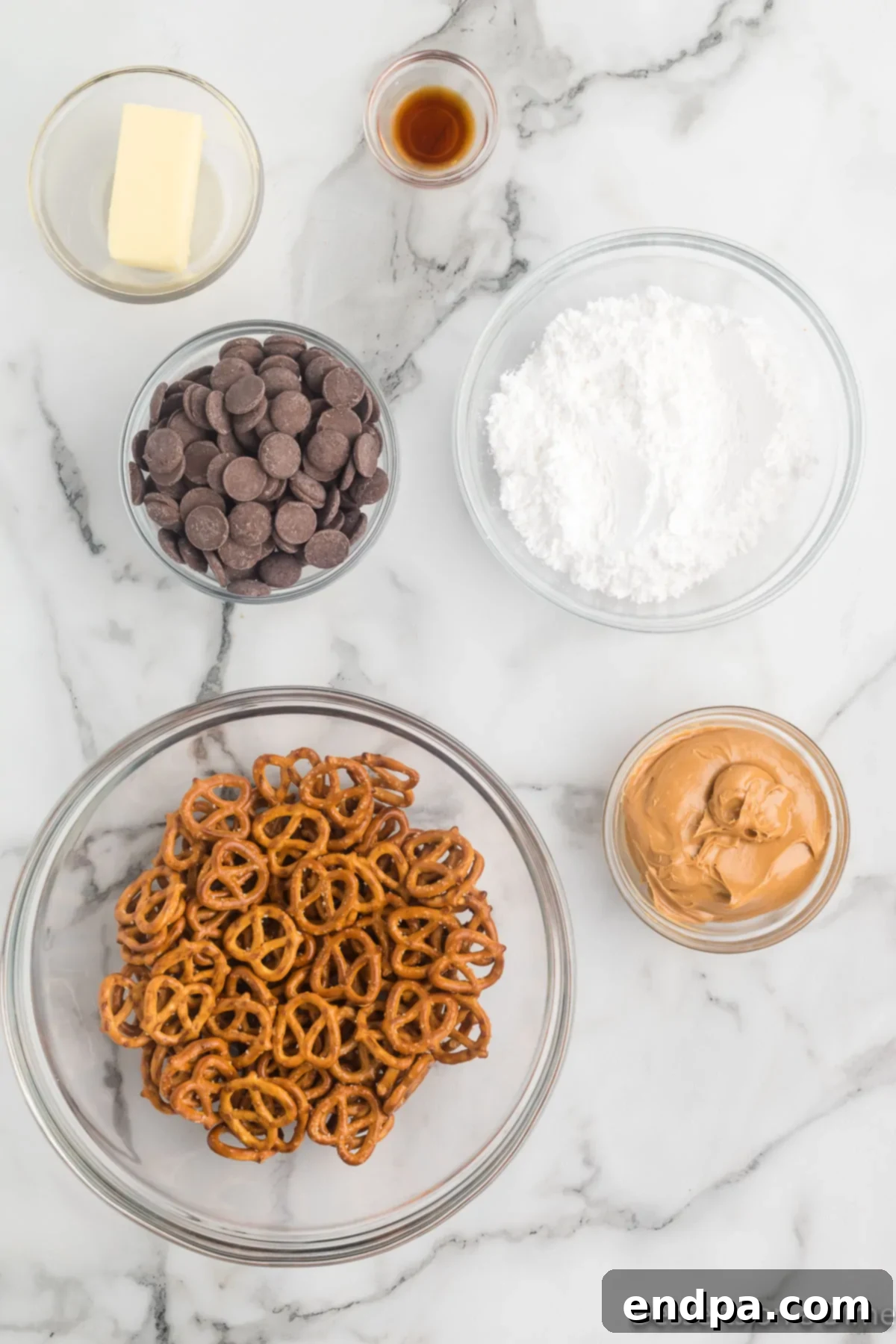 A visual display of all ingredients required for Peanut Butter Pretzel Bites: mini pretzels, creamy peanut butter, chocolate melting wafers, butter, and powdered sugar.
