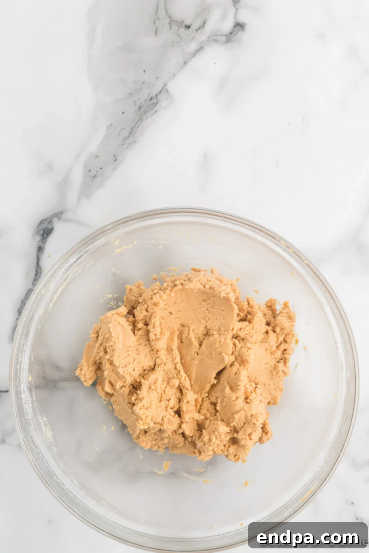 Mixing bowl with powdered sugar being gradually incorporated into the peanut butter and butter mixture, forming a cohesive dough.