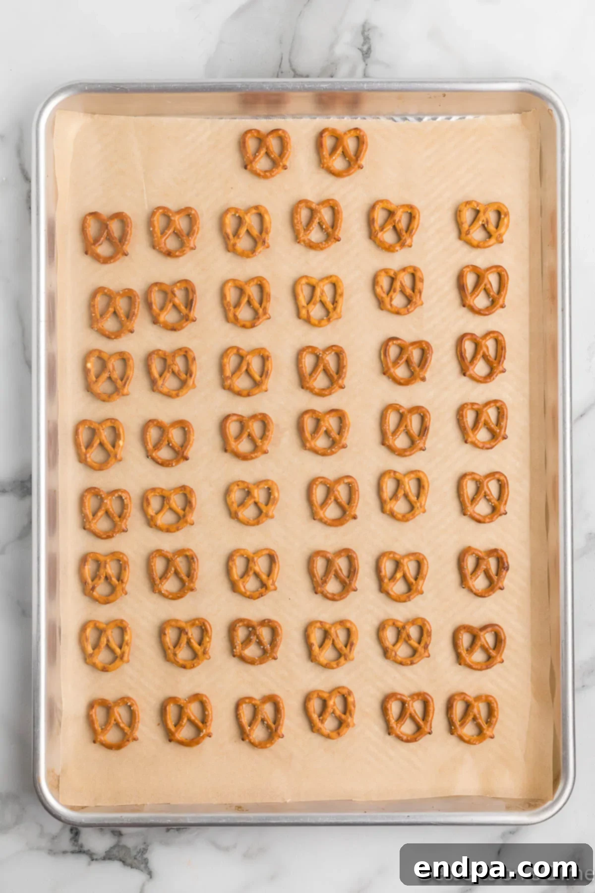 A baking sheet neatly lined with parchment paper, with mini twist pretzels spread out in a single layer.