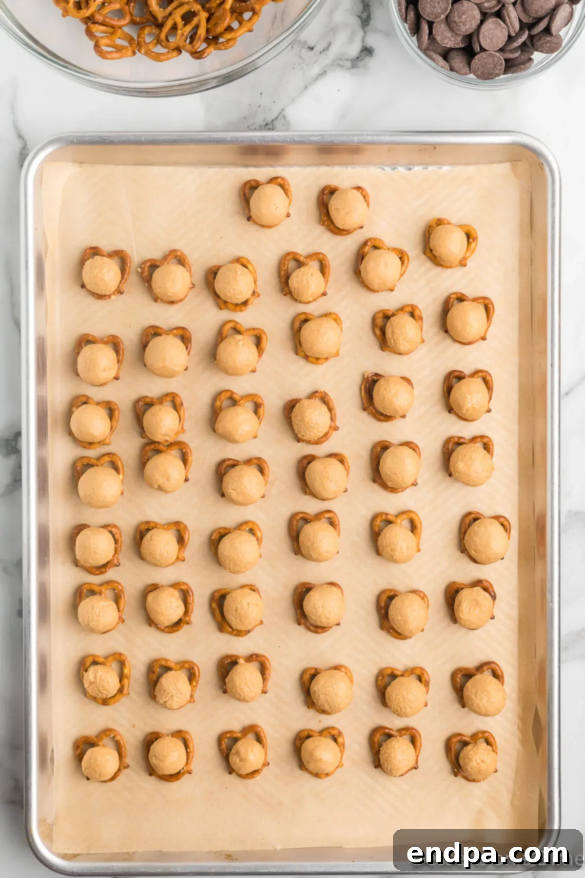Baking sheet showing pretzels topped with small, perfectly rolled peanut butter balls, ready for the top pretzel layer.