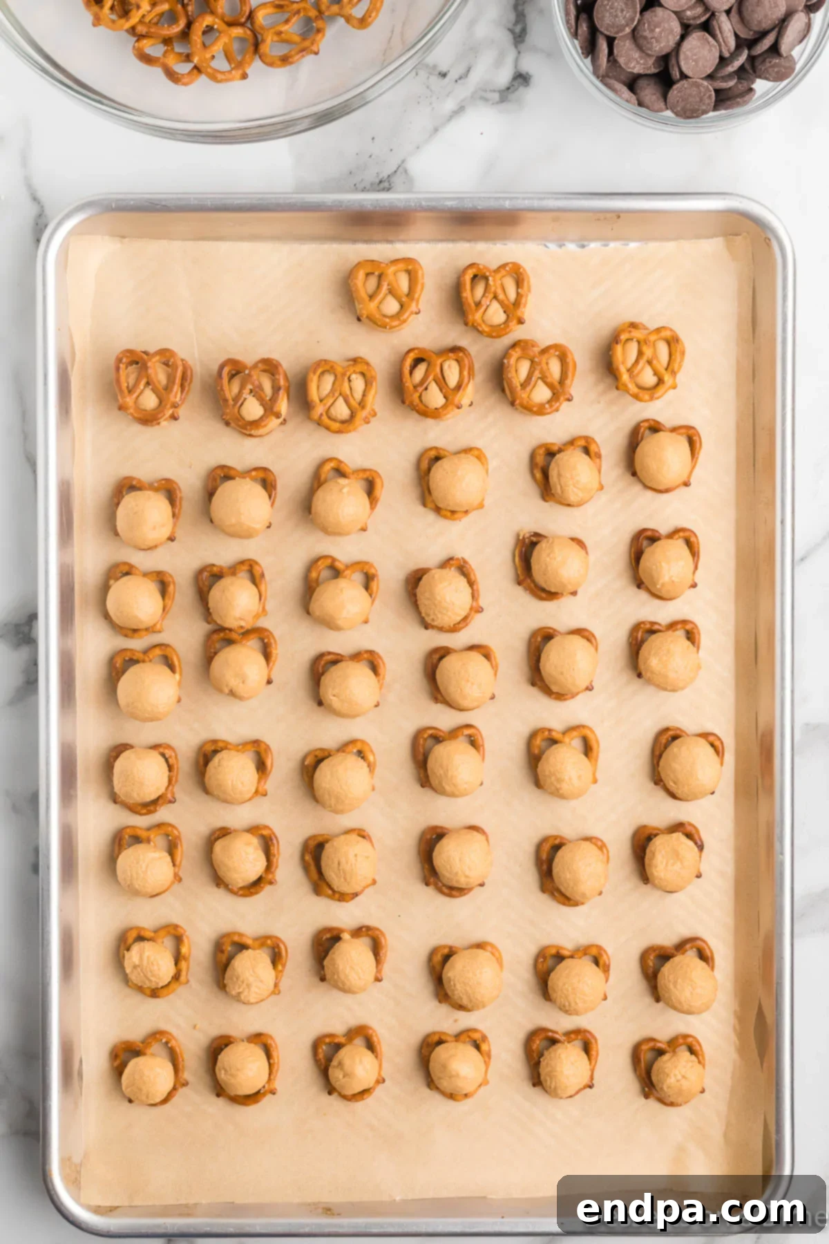 A hand gently pressing a second pretzel on top of a peanut butter ball that rests on another pretzel, forming a sandwich.