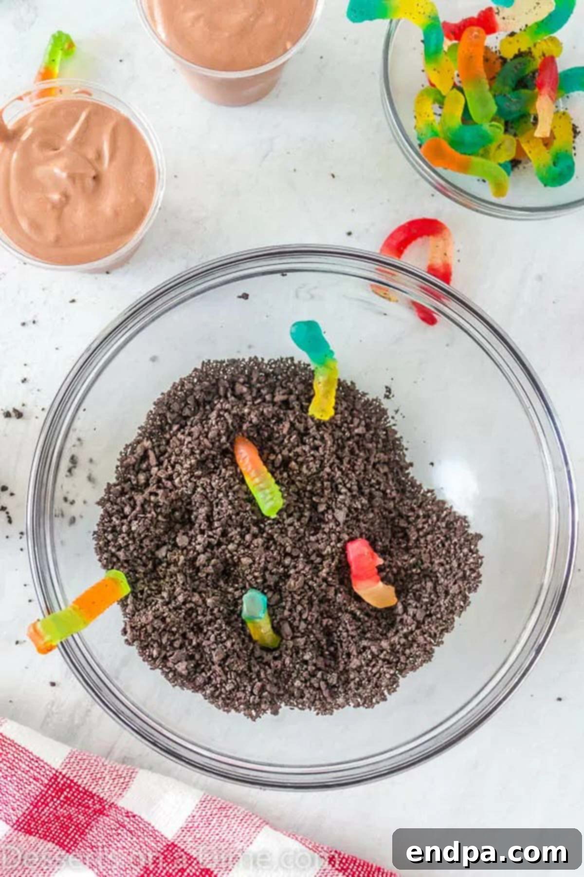 Delicious Dirt Cup Delight 5 Crushed Oreo cookies in a bowl, alongside a handful of colorful gummy worms, ready for layering.