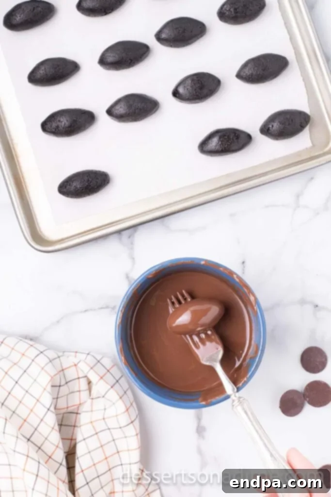 An Oreo ball being dipped into melted chocolate with a fork.