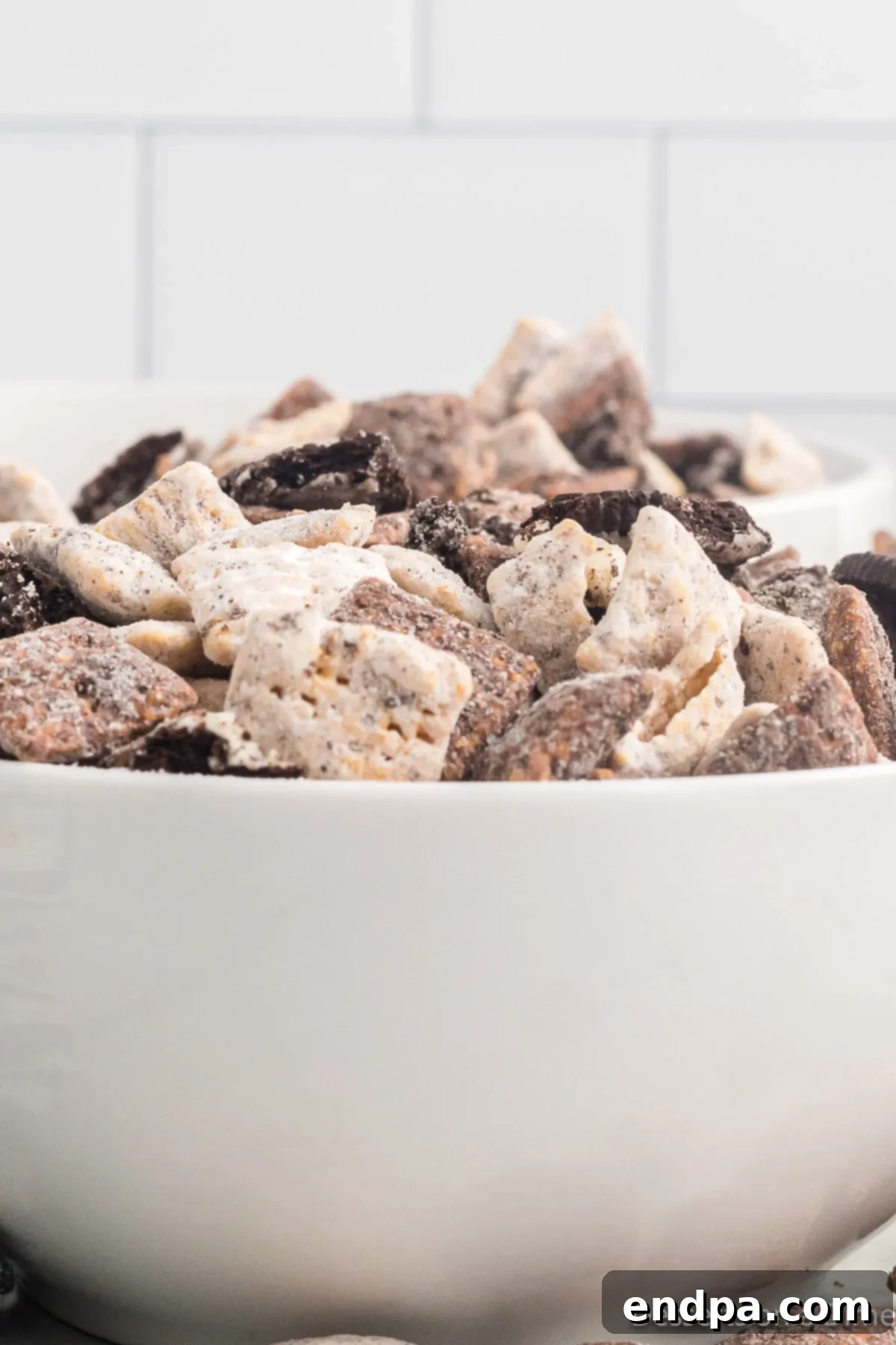 A bowl filled with delicious Cookies and Cream Muddy Buddies, showcasing the iconic black and white cookie crumbs and chocolate coating.