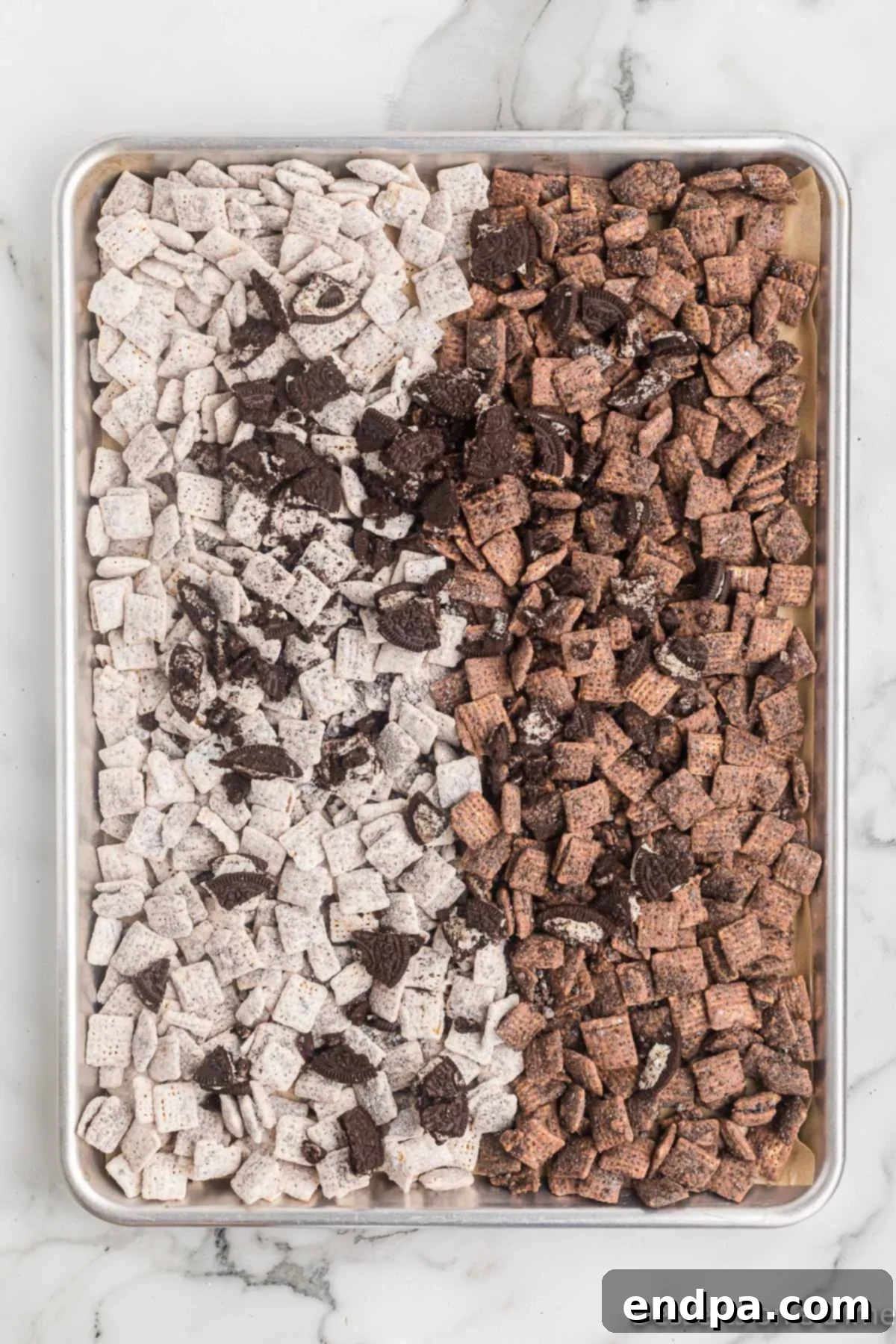 A baking sheet spread with both white chocolate and milk chocolate coated cereals, mixed with larger Oreo pieces, setting.