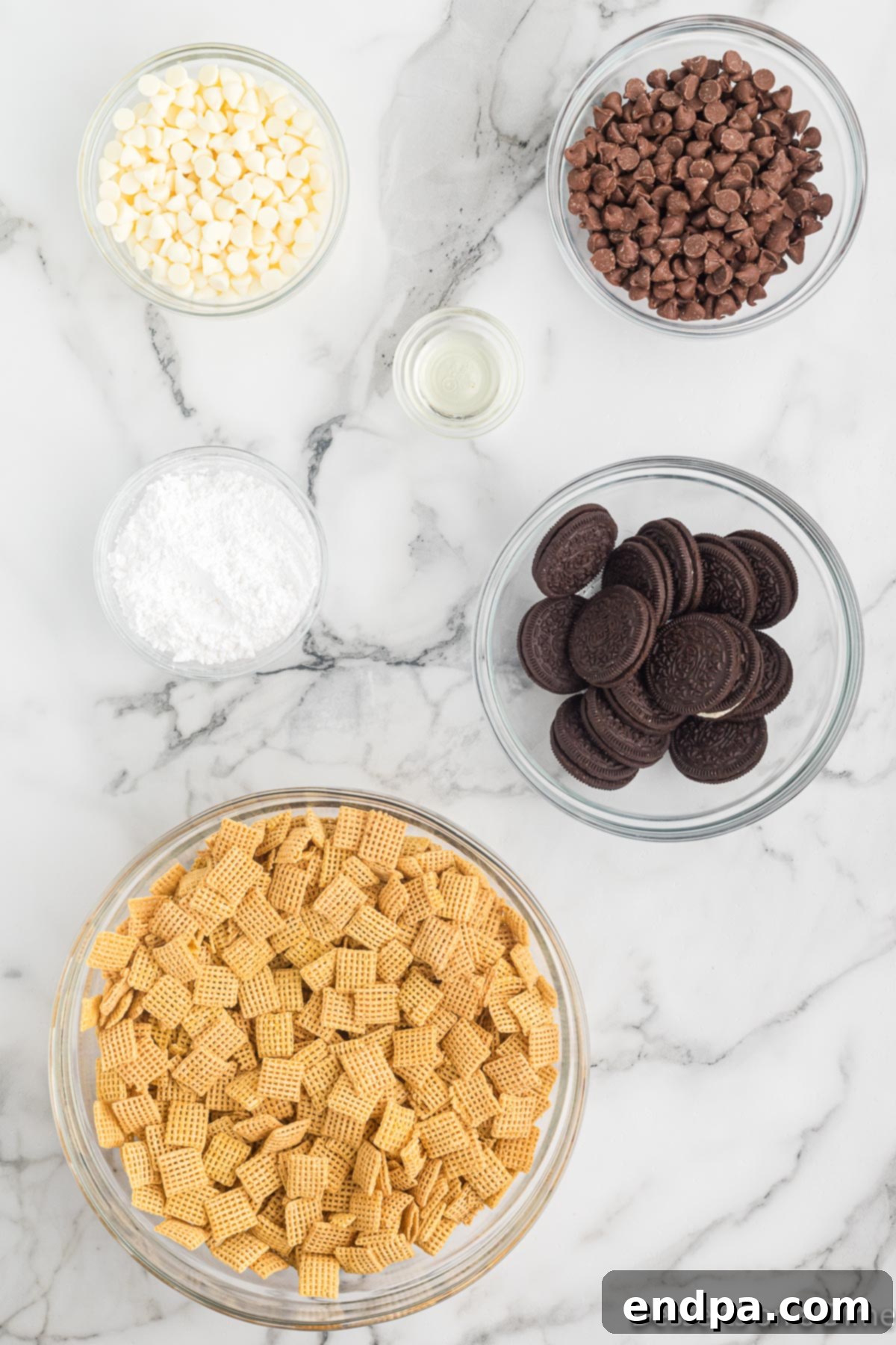 Ingredients for Cookies and Cream Muddy Buddies laid out: cereal, chocolate chips, Oreo cookies, vegetable oil, and powdered sugar.
