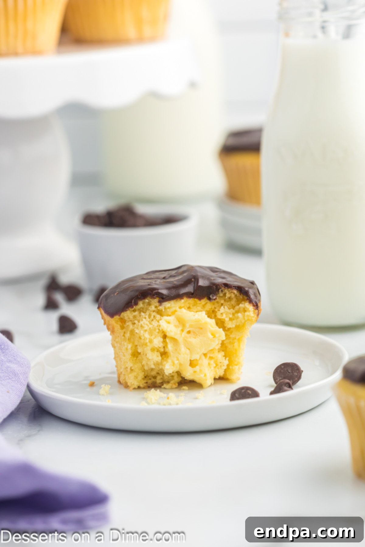 Gourmet Eclair Cupcakes 2 A perfectly halved Chocolate Eclair Cupcake, showcasing its creamy vanilla custard filling and rich chocolate ganache topping, resting on a white plate.