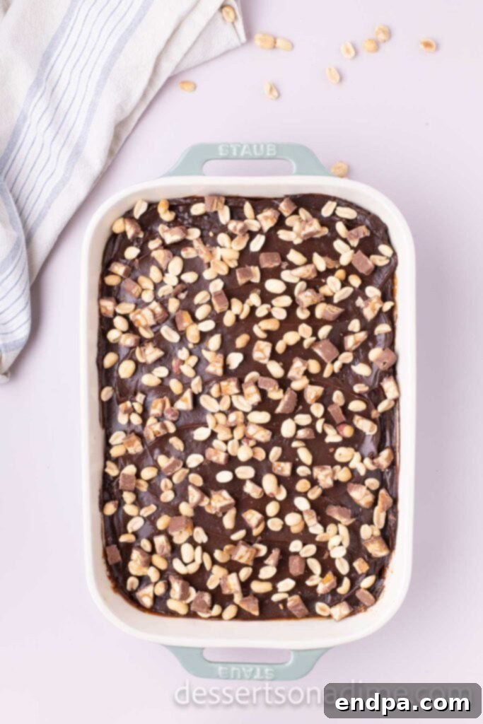 Snickers Overload Cake 11 The frosted Snickers cake topped with additional chopped peanuts and crushed Snickers candy bars, ready to be served.