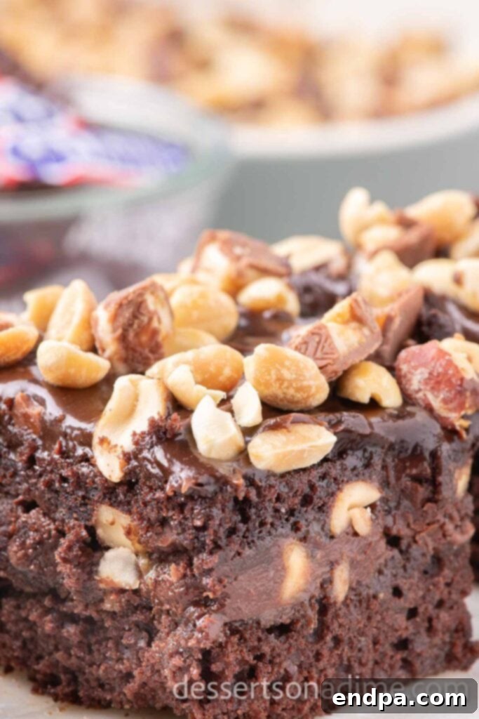 Snickers Overload Cake 12 A beautifully cut slice of Snickers cake, showing the layered structure, served on a white plate with a fork.