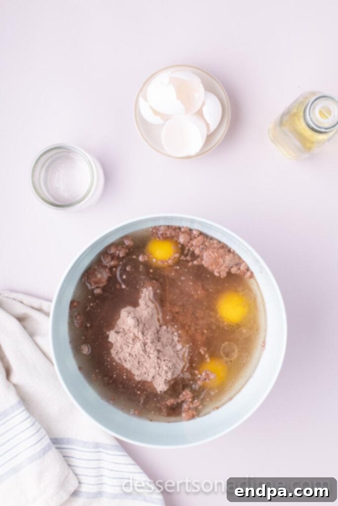 Snickers Overload Cake 4 Mixing bowl with cake mix, oil, eggs, and water being combined by a stand mixer.