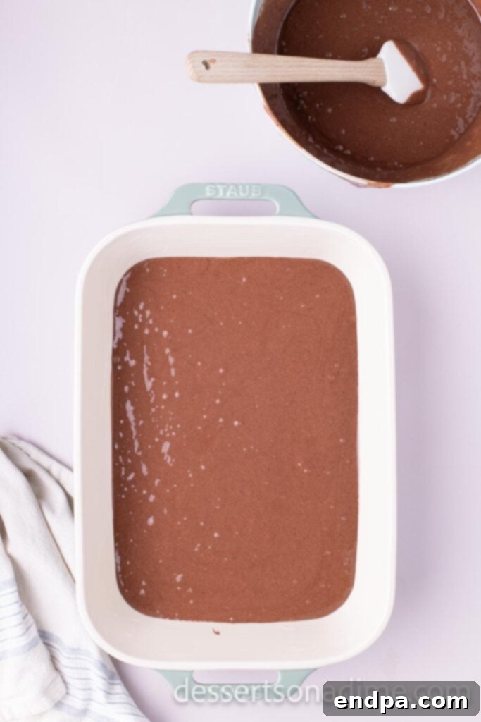 Snickers Overload Cake 5 Half of the chocolate cake batter poured into a prepared 9x13 inch cake pan, ready for the first bake.