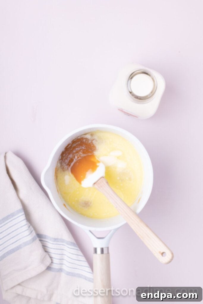 Snickers Overload Cake 6 A saucepan on the stove with caramel candies, milk, and butter melting together over medium heat.