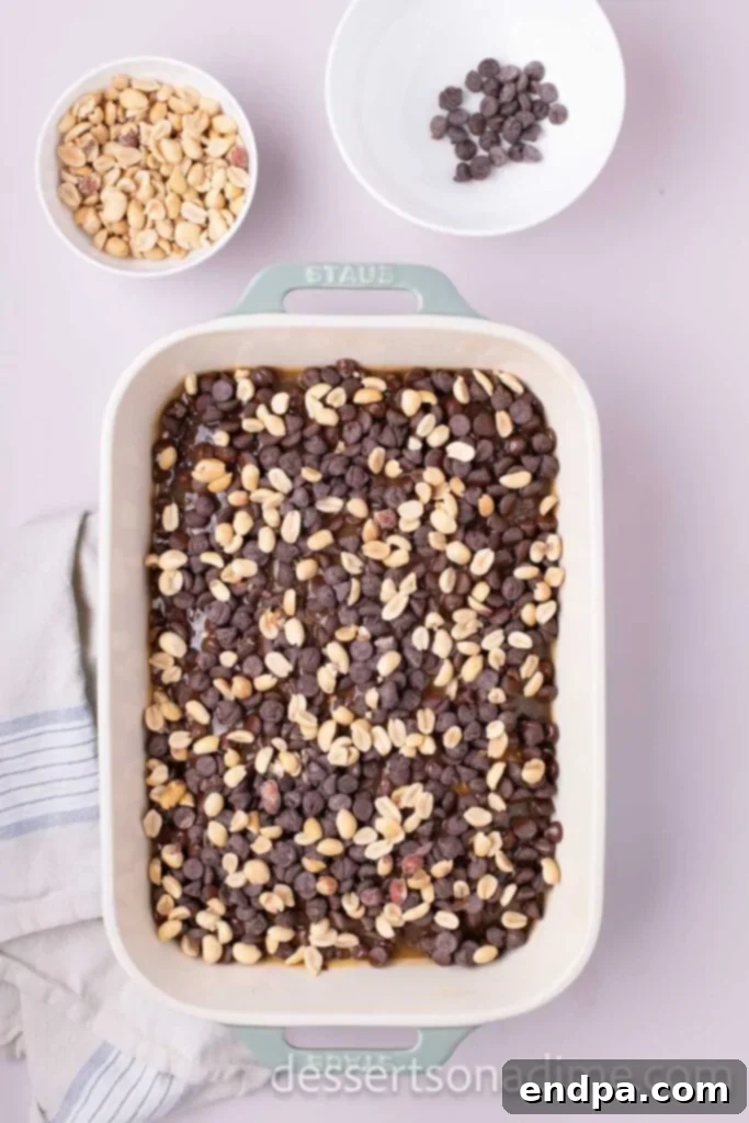 Snickers Overload Cake 8 Chocolate chips and chopped peanuts sprinkled generously over the warm caramel layer of the partially baked cake.