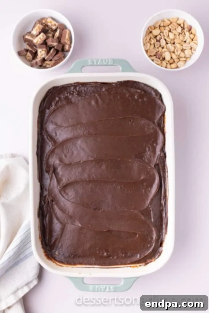 Snickers Overload Cake 10 Chocolate frosting smoothly spread over the cooled Snickers cake, ready for final toppings.