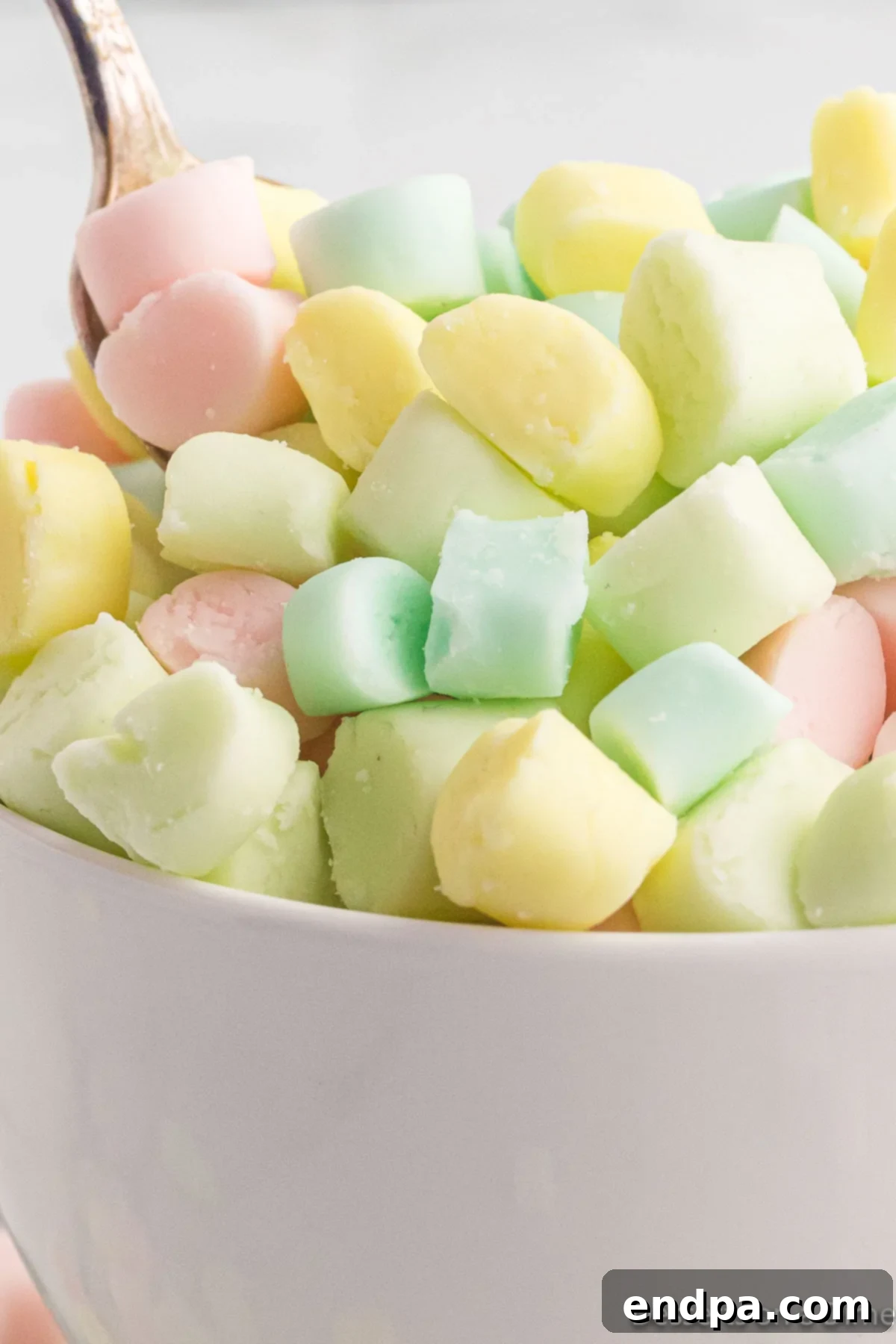 Creamy Mint Delights 9 A close-up of a bowl filled with various colored, dried butter mints, with a small spoon resting inside, ready for serving.