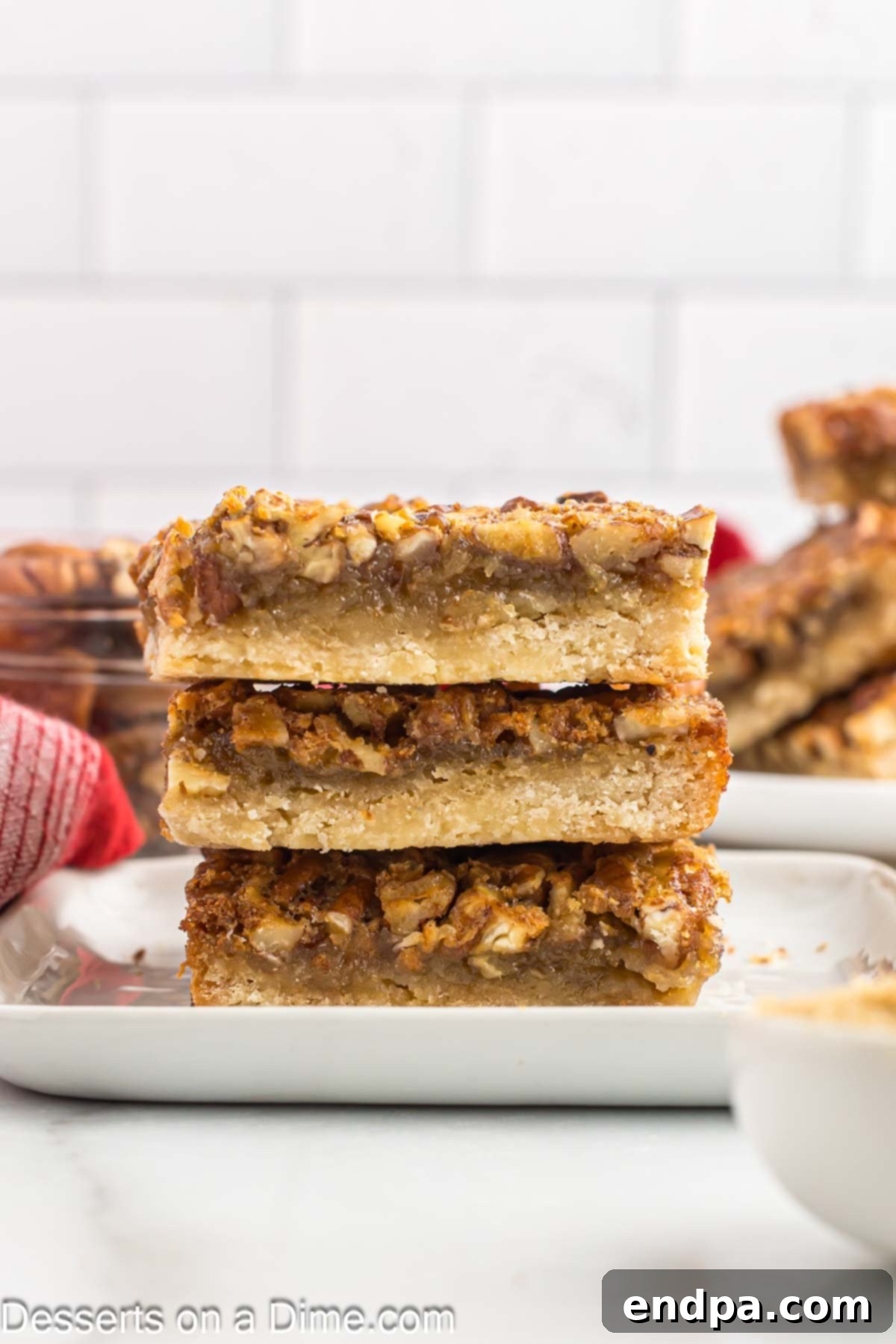 Perfectly cut Pecan Pie Bars stacked elegantly on a white plate, showcasing their inviting layers and rich texture.