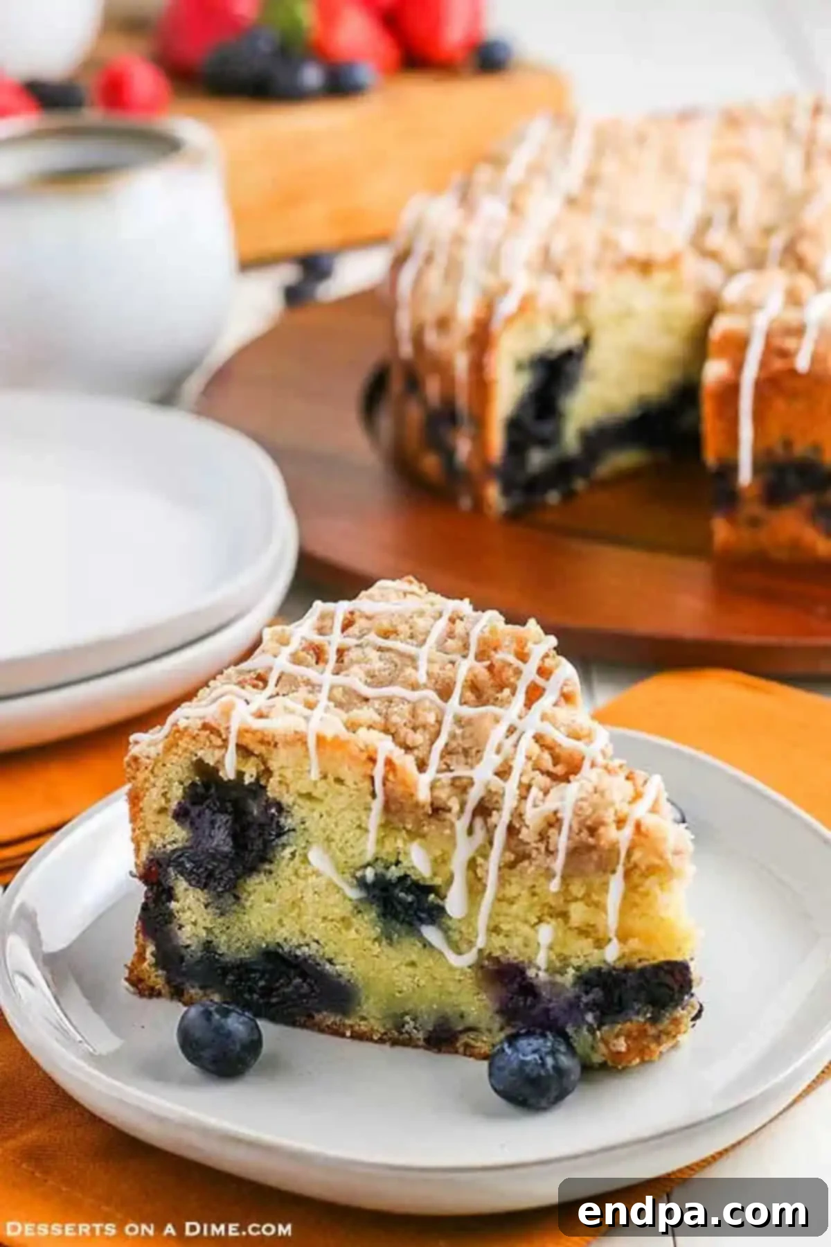A generous slice of moist blueberry coffee cake, topped with golden crumb and a sweet white glaze, served on a pristine white plate, invitingly ready to be enjoyed.