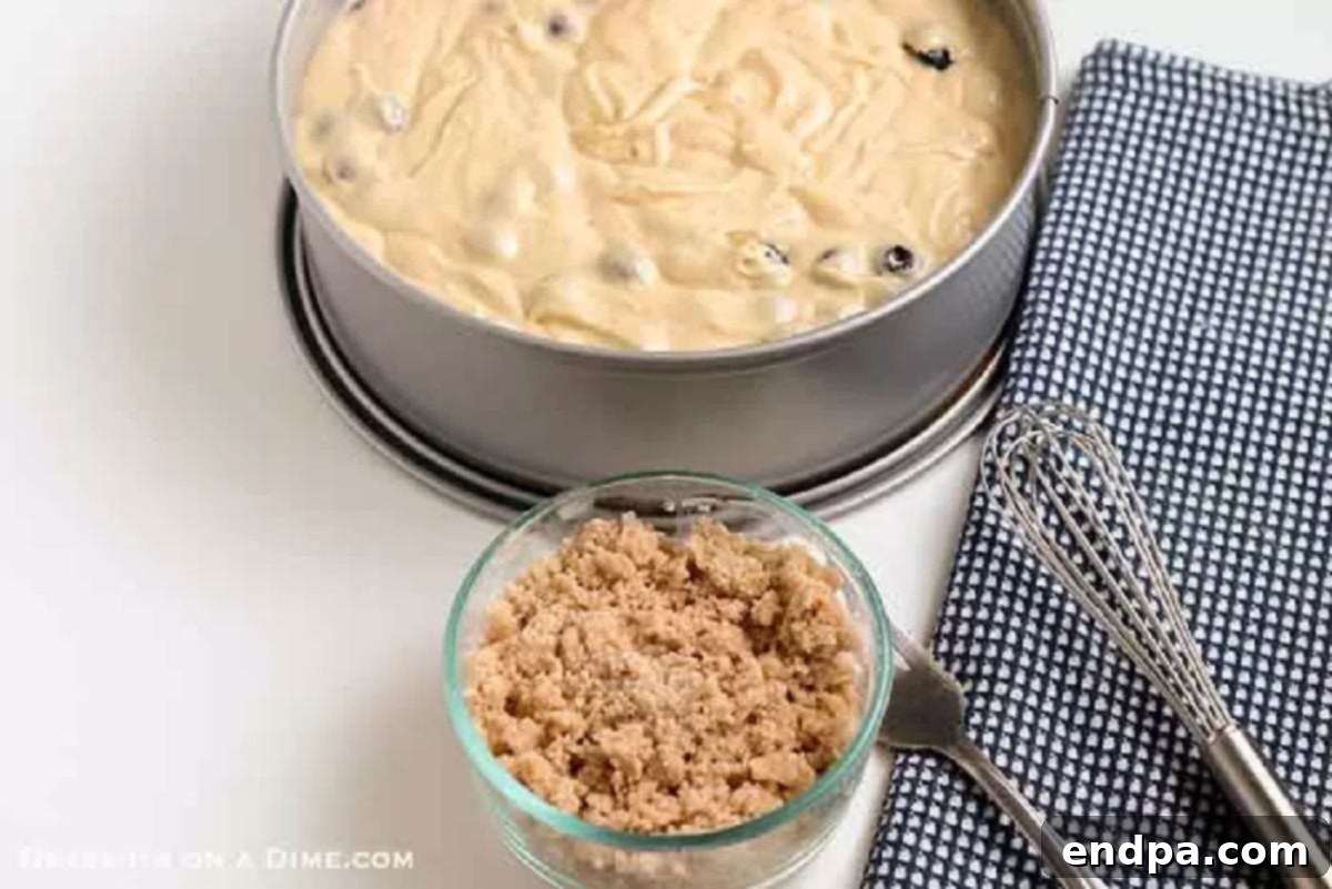Smooth coffee cake batter, studded with blueberries, carefully poured into a prepared baking pan, ready for the crumb topping.