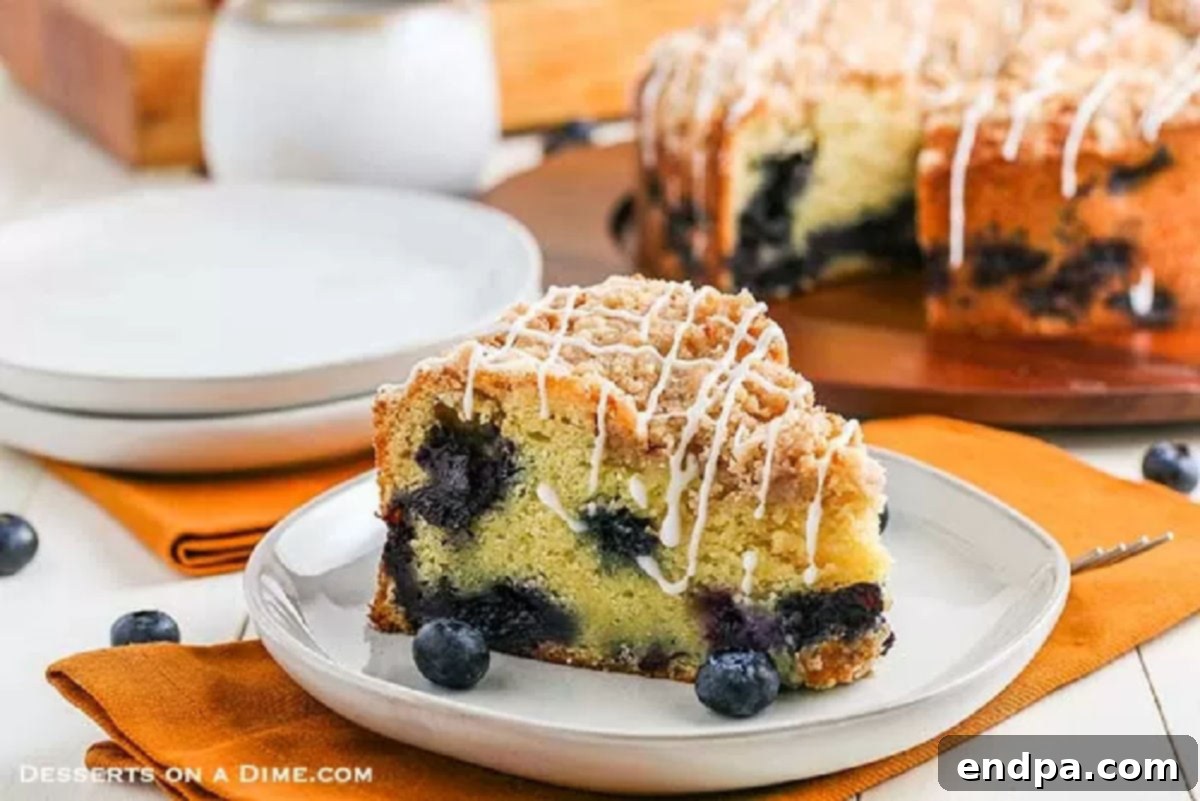 A freshly baked slice of blueberry coffee cake, still warm and glistening with a sweet glaze, presented on a white plate, ready to be enjoyed.