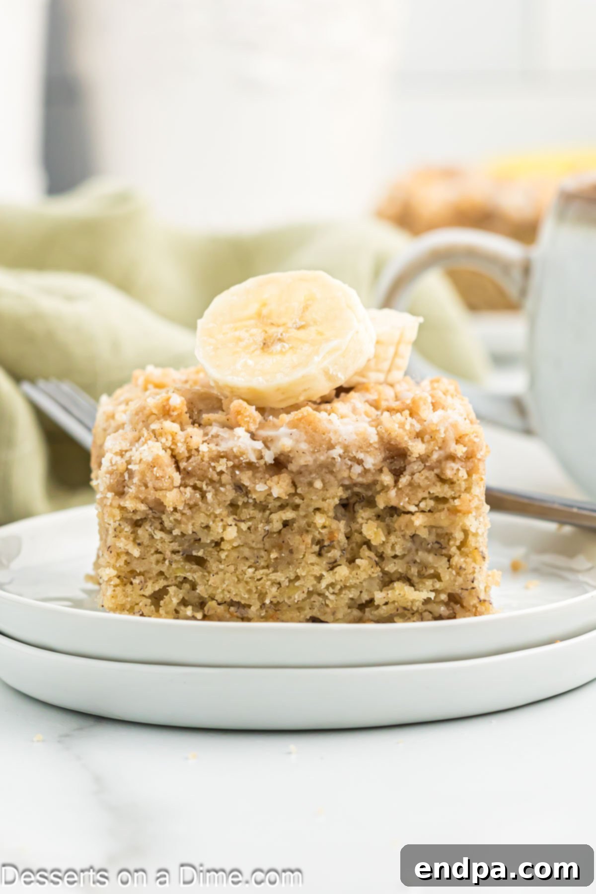 A beautiful slice of moist banana coffee cake on a white plate, showcasing its fluffy texture, golden streusel topping, and elegant vanilla glaze drizzle, ready to be savored.