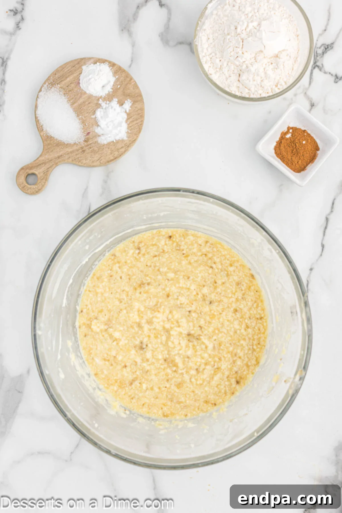 A close-up of a mixing bowl with mashed bananas, a cracked egg, a dollop of sour cream, and a splash of vanilla extract, all combined.