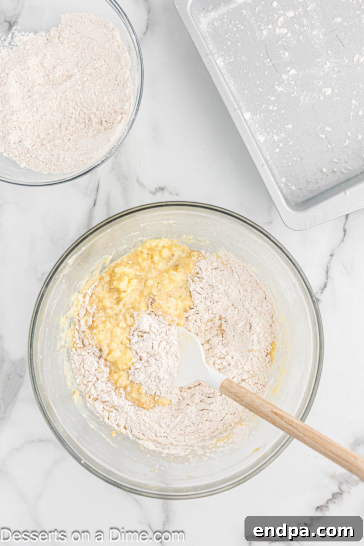 The mixing bowl with wet ingredients now combined with the dry ingredients, showing a thick, pale yellow batter that is just mixed.