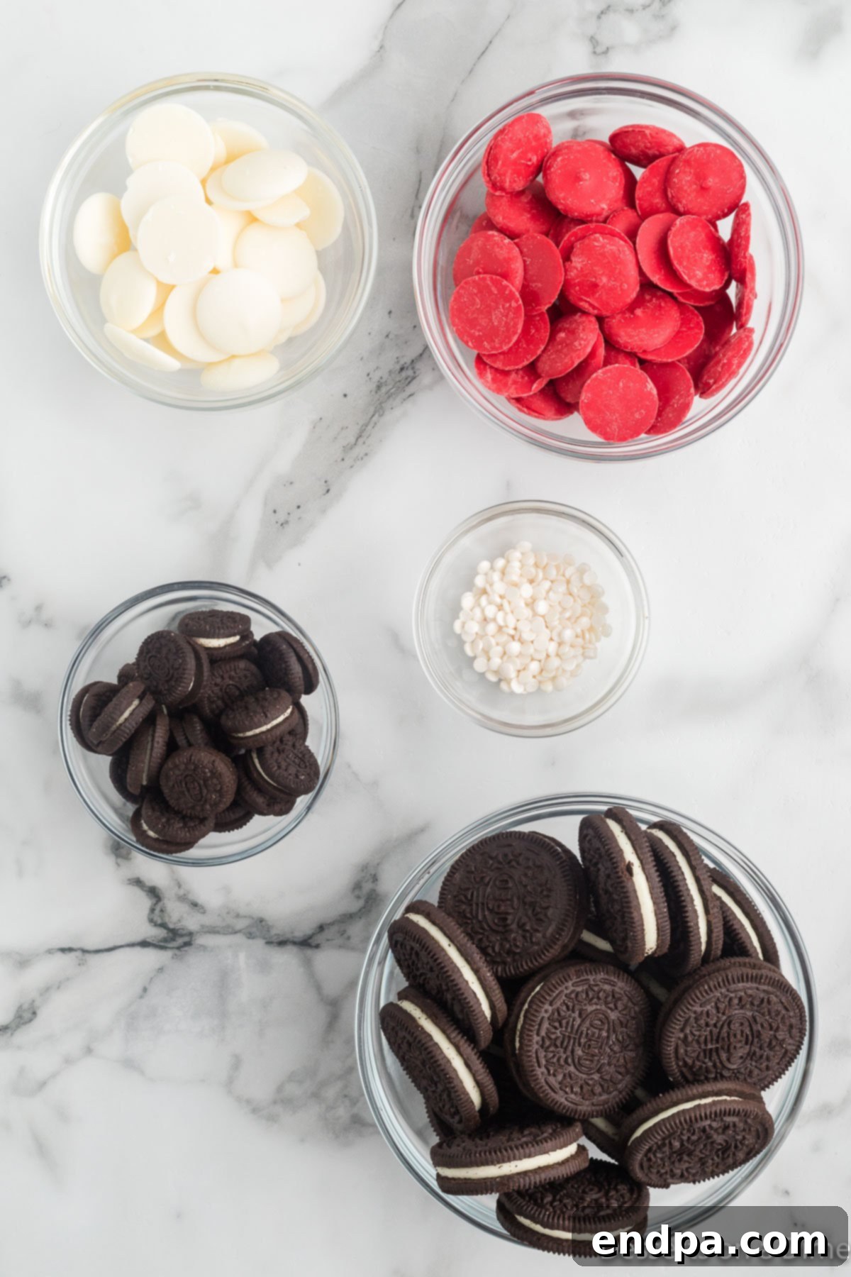Mickey's Magical Oreo Treats 3 A selection of ingredients for Mickey Mouse Oreo Cookies: colorful red and white candy melts, classic Double Stuffed Oreo cookies, mini Oreo cookies, and white circular sprinkles.