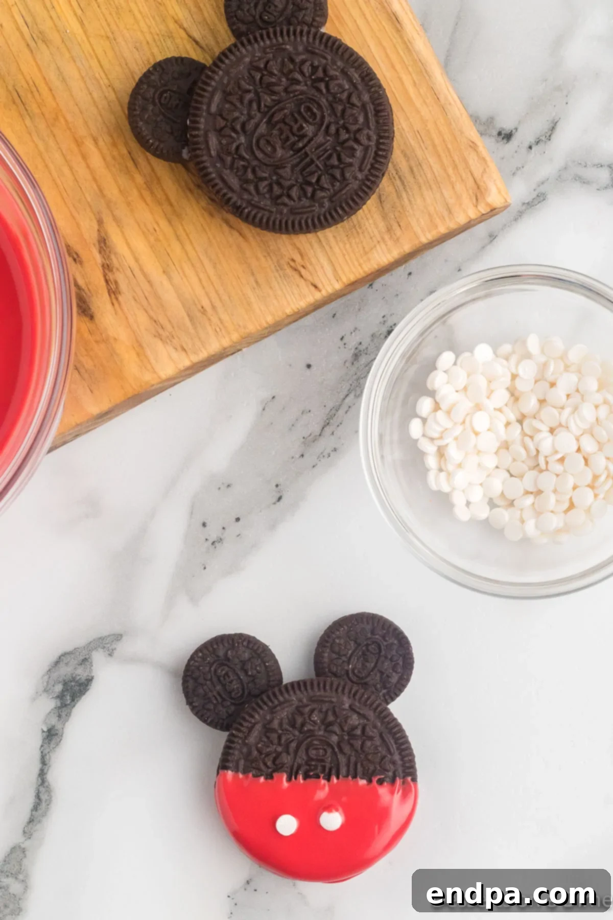Mickey's Magical Oreo Treats 8 A Mickey Mouse Oreo cookie, freshly dipped in red candy melts, with two small white circular sprinkles meticulously added to represent his classic buttons.