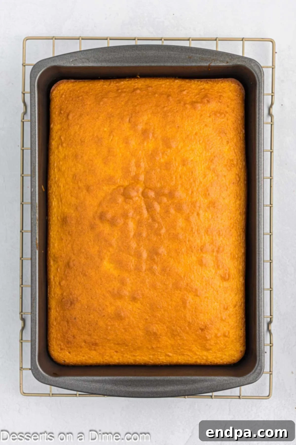 A freshly baked yellow cake in a 9x13 inch baking pan, cooling after being removed from the oven.