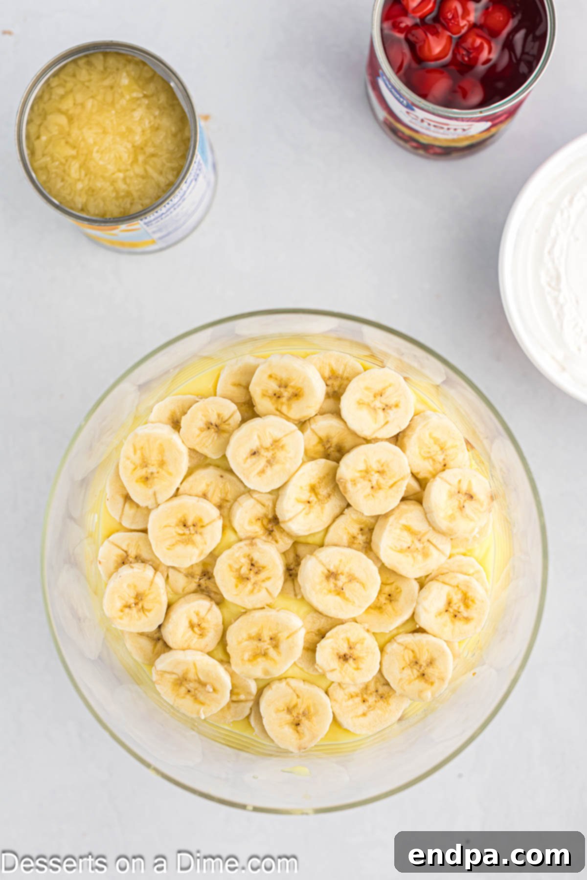 The first layer of Punch Bowl Cake in a trifle dish, showing neatly arranged banana slices over a pudding base.