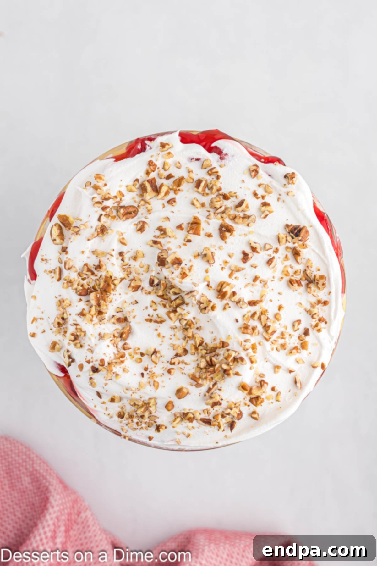 The final layers of Punch Bowl Cake being assembled, with whipped cream generously spread and chopped pecans sprinkled on top.