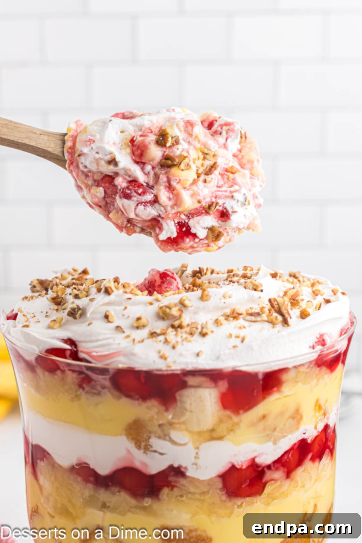 A spoon scooping a generous portion of Punch Bowl Cake out of a clear glass trifle dish, showing the beautiful layers.