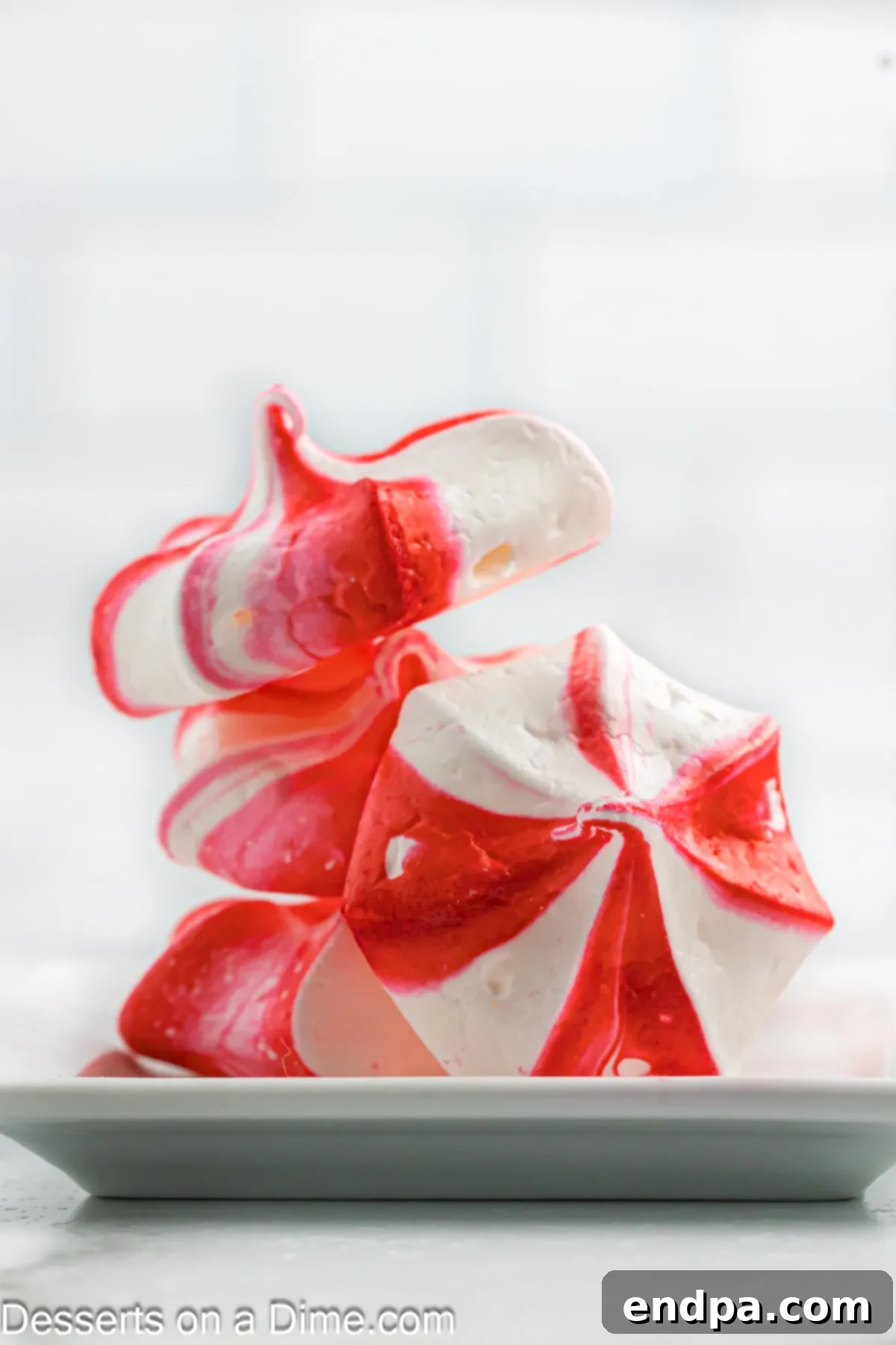 Peppermint Cloud Kisses 2 Stacked peppermint meringue cookies on a festive platter, showcasing their red and white stripes and delicate appearance.