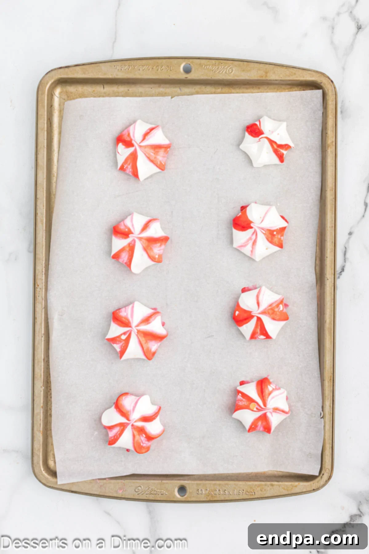 Peppermint Cloud Kisses 7 Small star-shaped peppermint meringue cookies piped onto a baking sheet lined with parchment paper.
