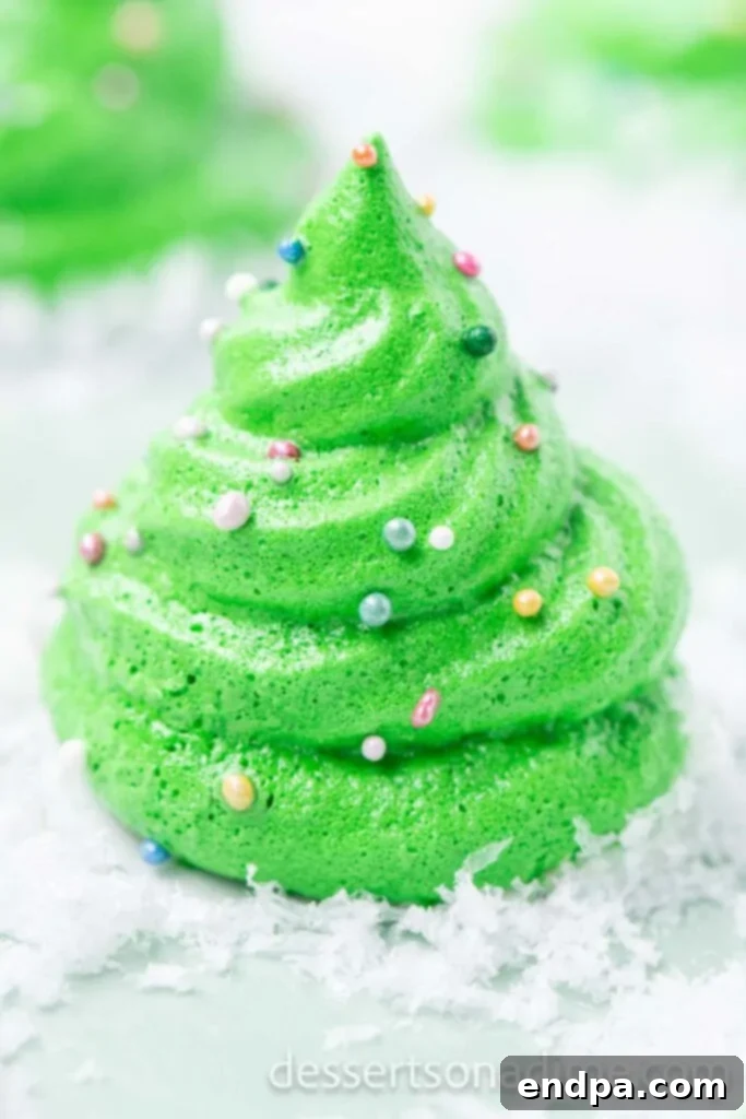 Festive Meringue Christmas Trees 10 Christmas treen cookie on a platter surrounded by powdered sugar.