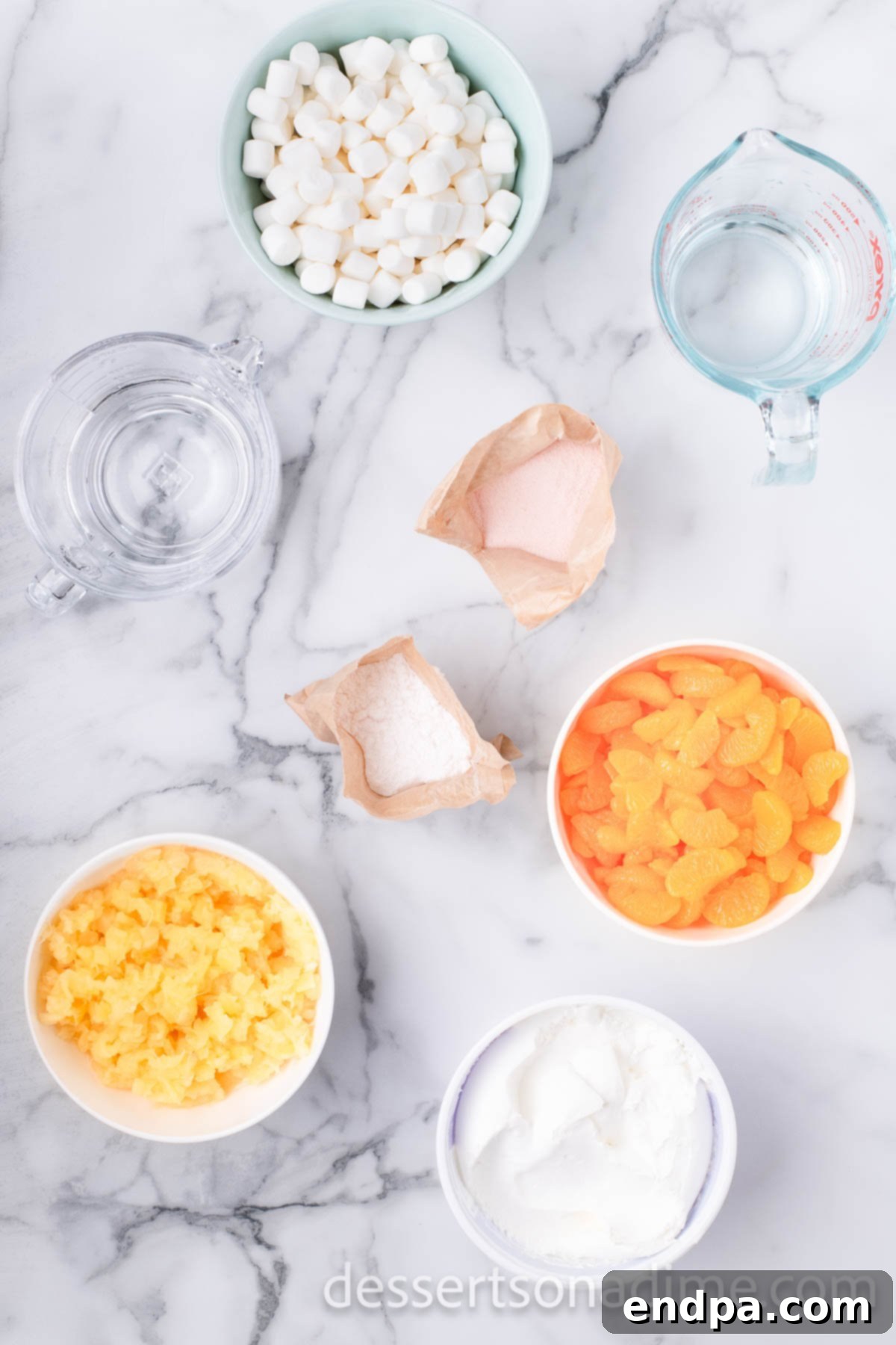 A selection of ingredients for orange fluff: bags of mini marshmallows, canned mandarin oranges, canned crushed pineapple, a tub of whipped topping, and instant pudding mix packets.