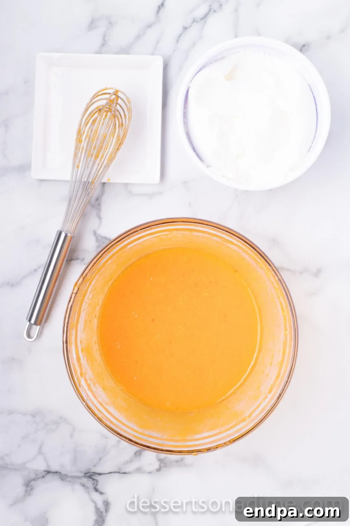 A bowl containing the dissolved orange Jell-O mixture, now with cold water added, resting in the refrigerator.