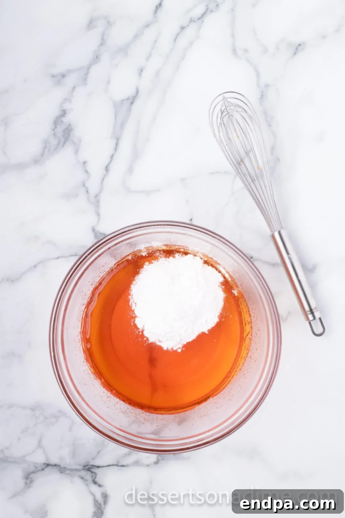 Instant vanilla pudding mix being stirred into the partially set orange Jell-O mixture with a whisk.