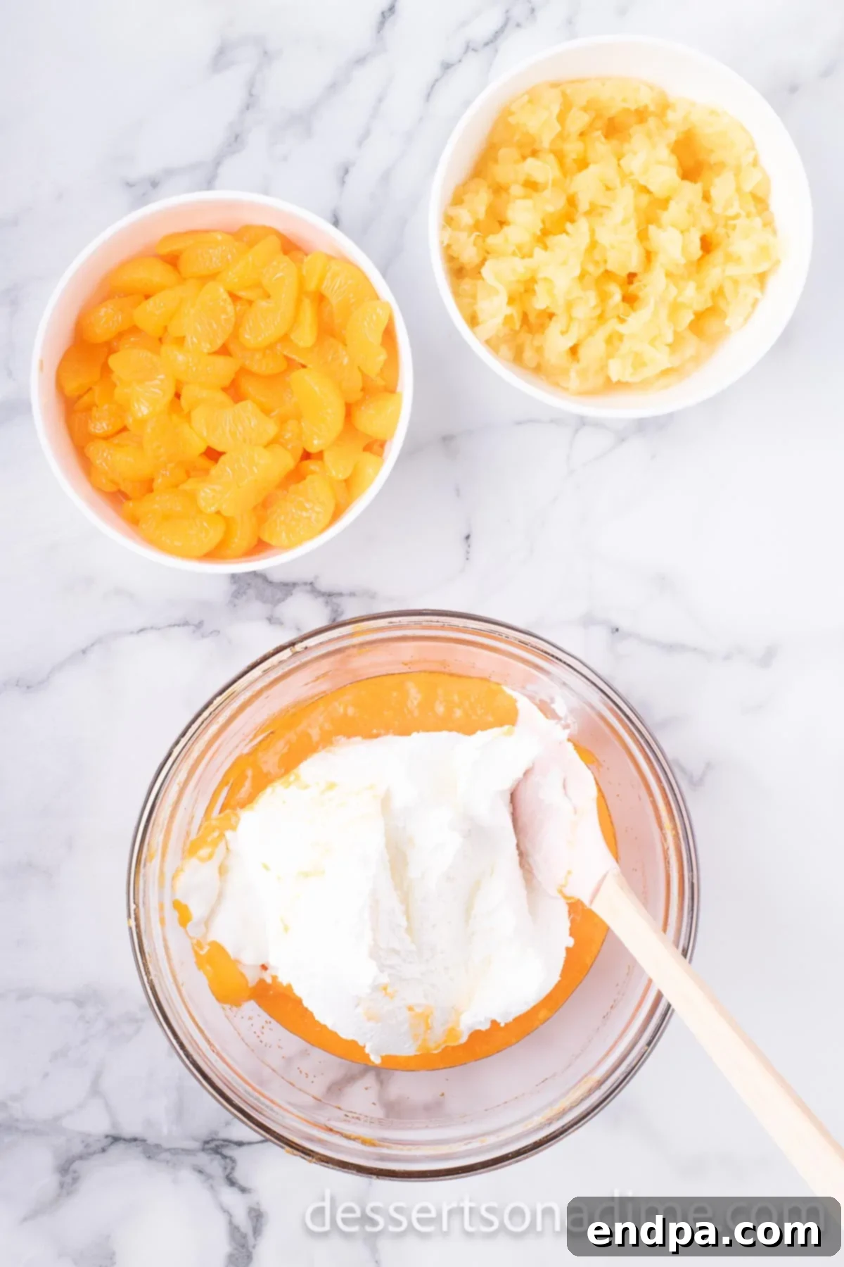 Thawed whipped topping being gently folded into the Jell-O and pudding mixture using a spatula, creating a light and airy consistency.