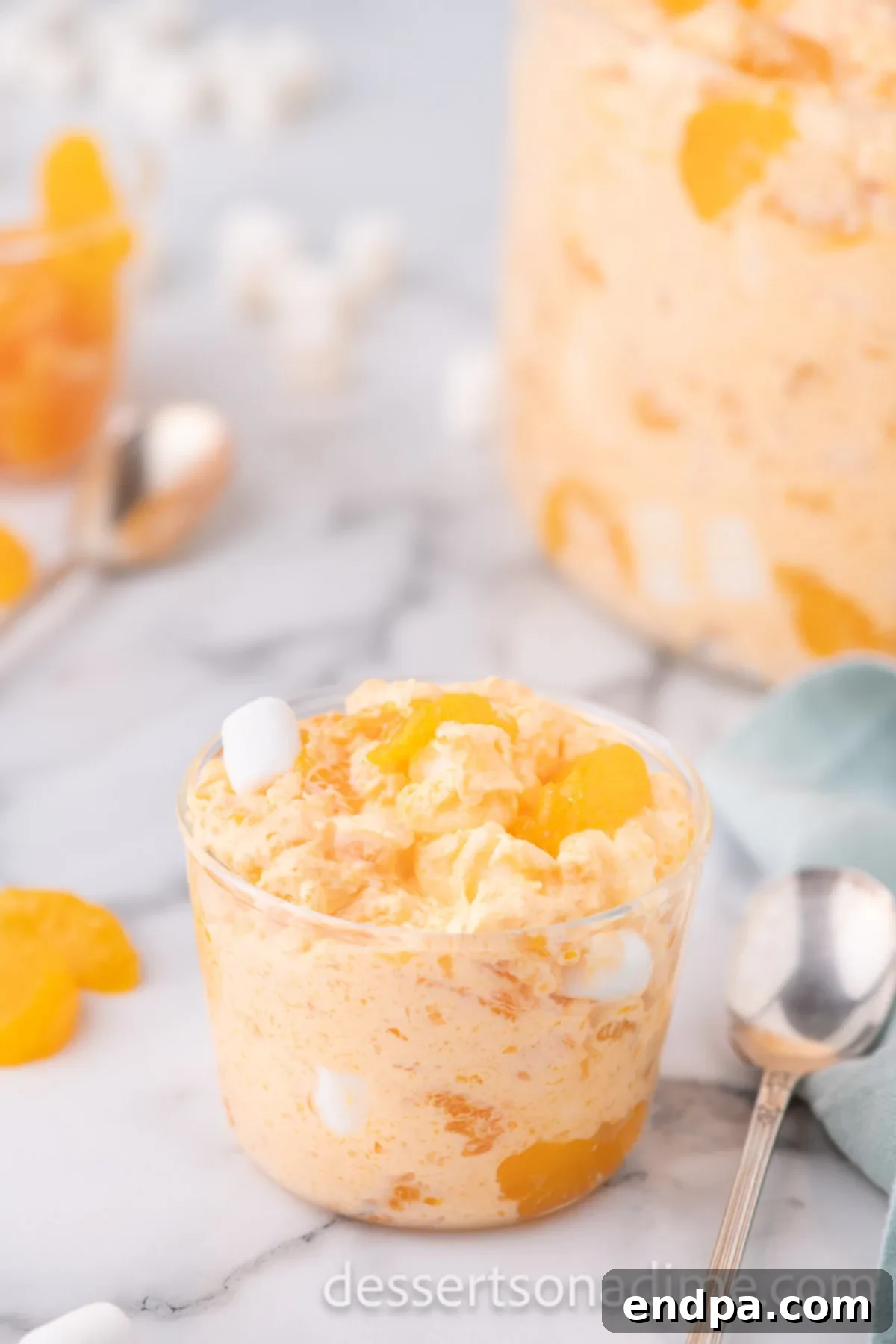 An individual serving of Orange Fluff presented in a small glass cup, ready to be enjoyed as a refreshing dessert.
