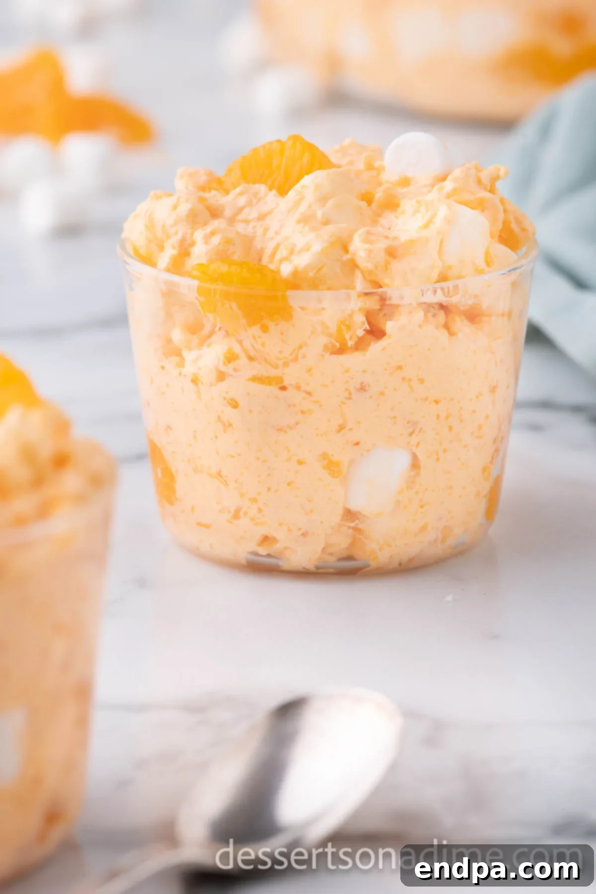 A close-up shot of a single cup of Orange Fluff, showcasing its creamy and fluffy texture, with visible pieces of mandarin orange and mini marshmallows, ready to be eaten.