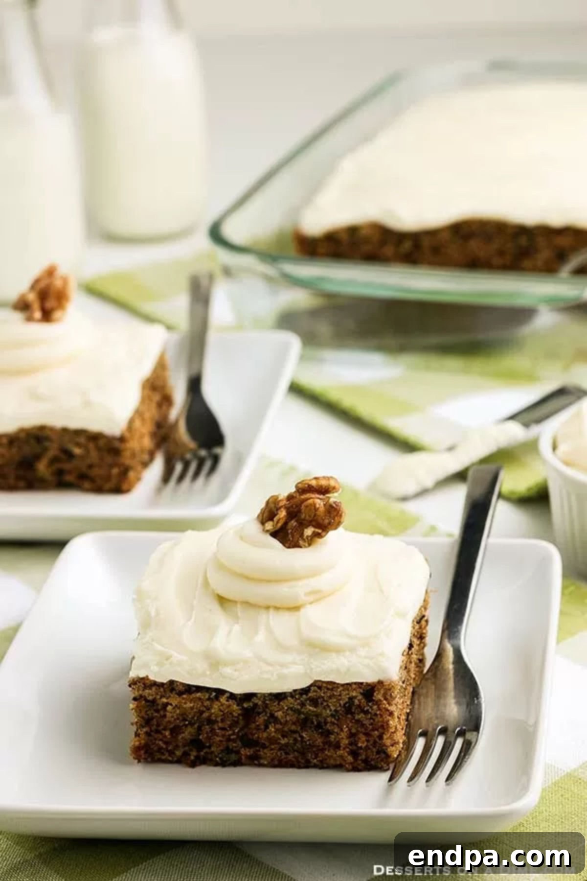 Slices of incredibly moist Zucchini Cake with creamy white frosting on a white plate, garnished with a sprinkle of cinnamon
