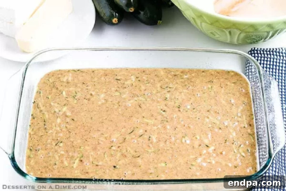 Smooth zucchini cake batter poured evenly into a prepared 13x9 inch baking dish, ready for the oven.
