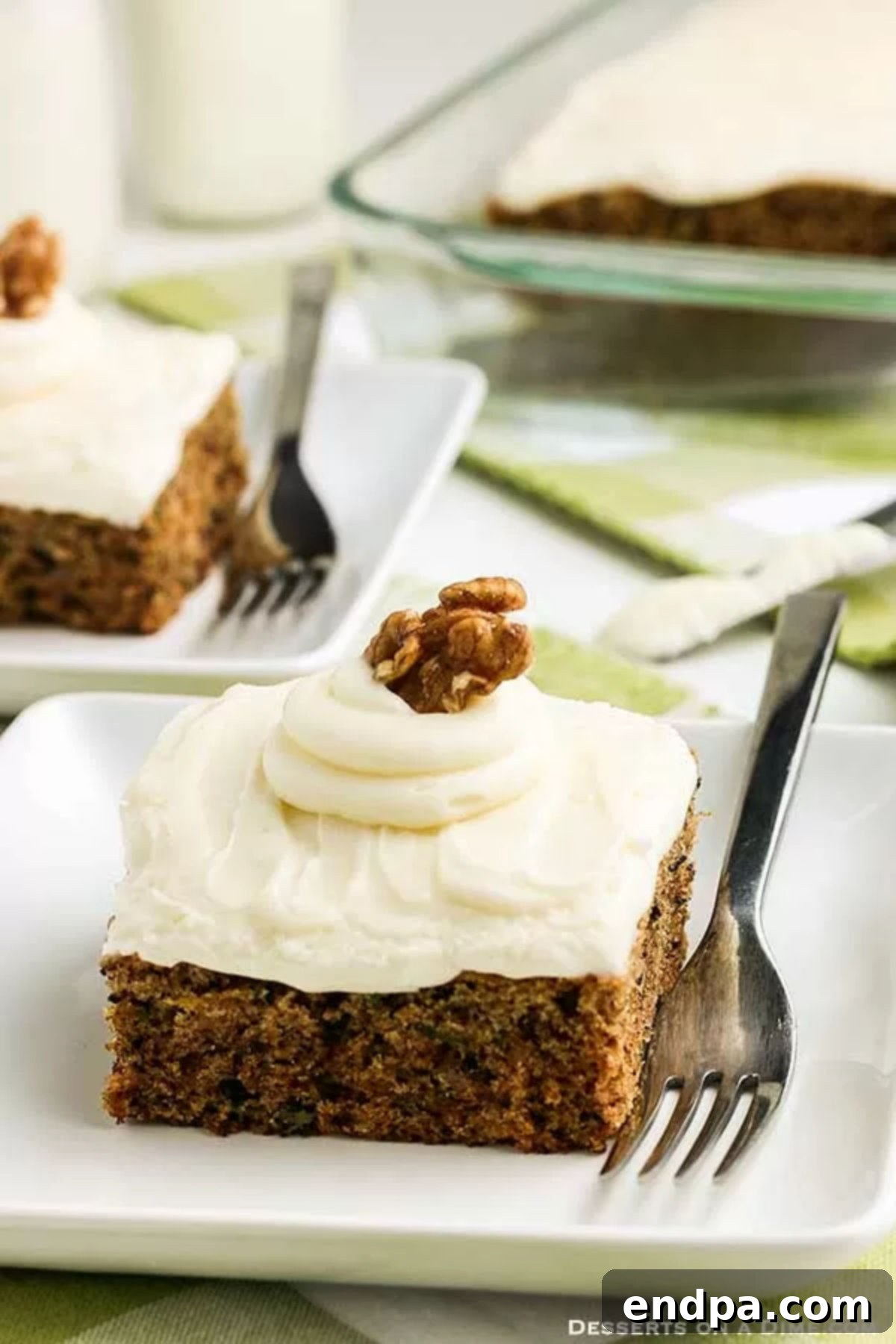 Several moist slices of Zucchini Cake with thick cream cheese frosting arranged on a clean white plate, ready to be enjoyed.