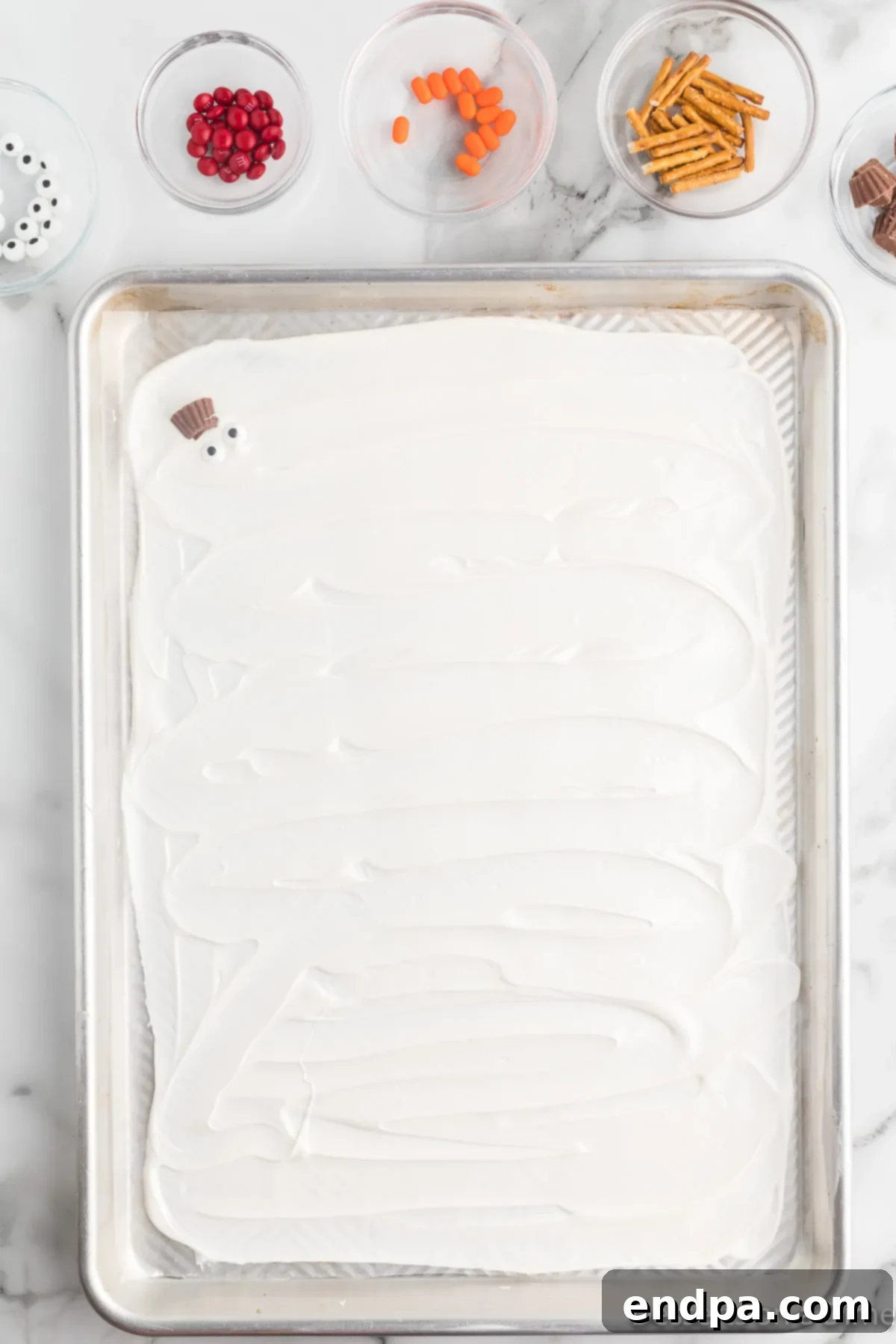 Frosty Meltdown Bark 6 Mini Reese's Peanut Butter Cups being arranged as snowman hats on the melted chocolate.