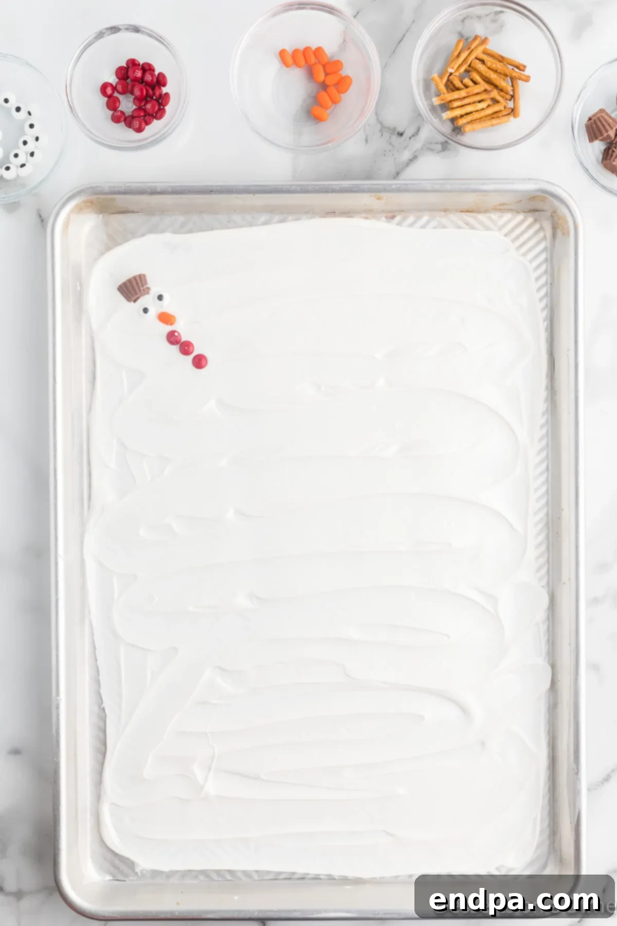 Frosty Meltdown Bark 7 Various candy pieces, including candy eyes, Tic Tacs, and Mini M&Ms, arranged to form snowman faces and buttons.