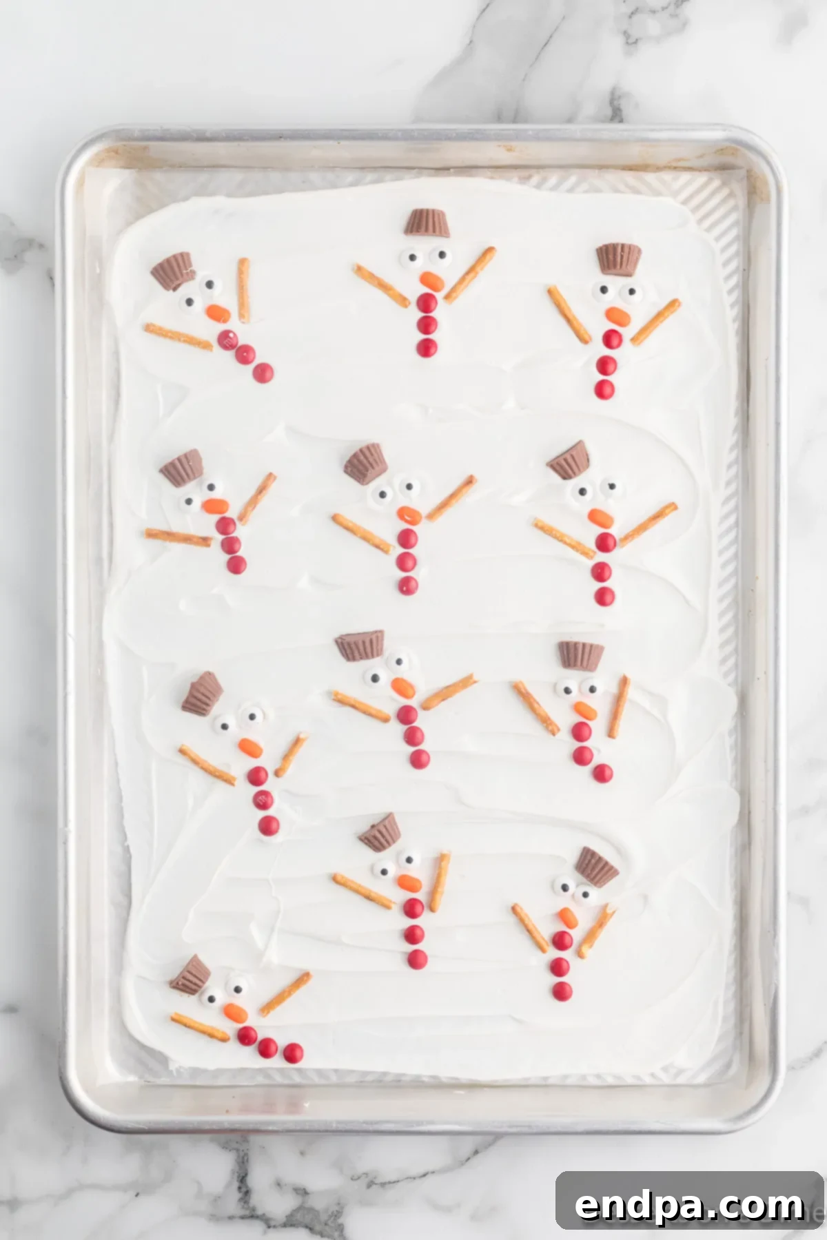 Frosty Meltdown Bark 9 A baking sheet filled with an array of completed melted snowmen on a white chocolate base, ready for chilling.