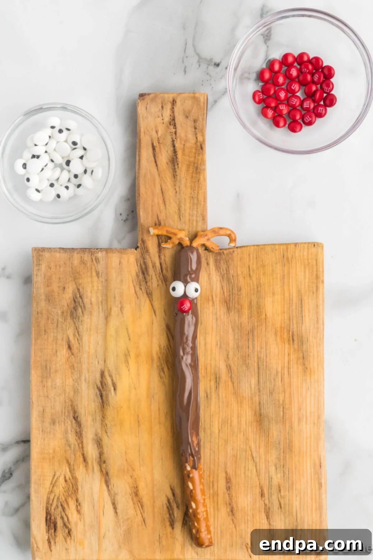 Broken pretzel twists being inserted into the still-wet chocolate coating of a pretzel rod to create reindeer antlers.