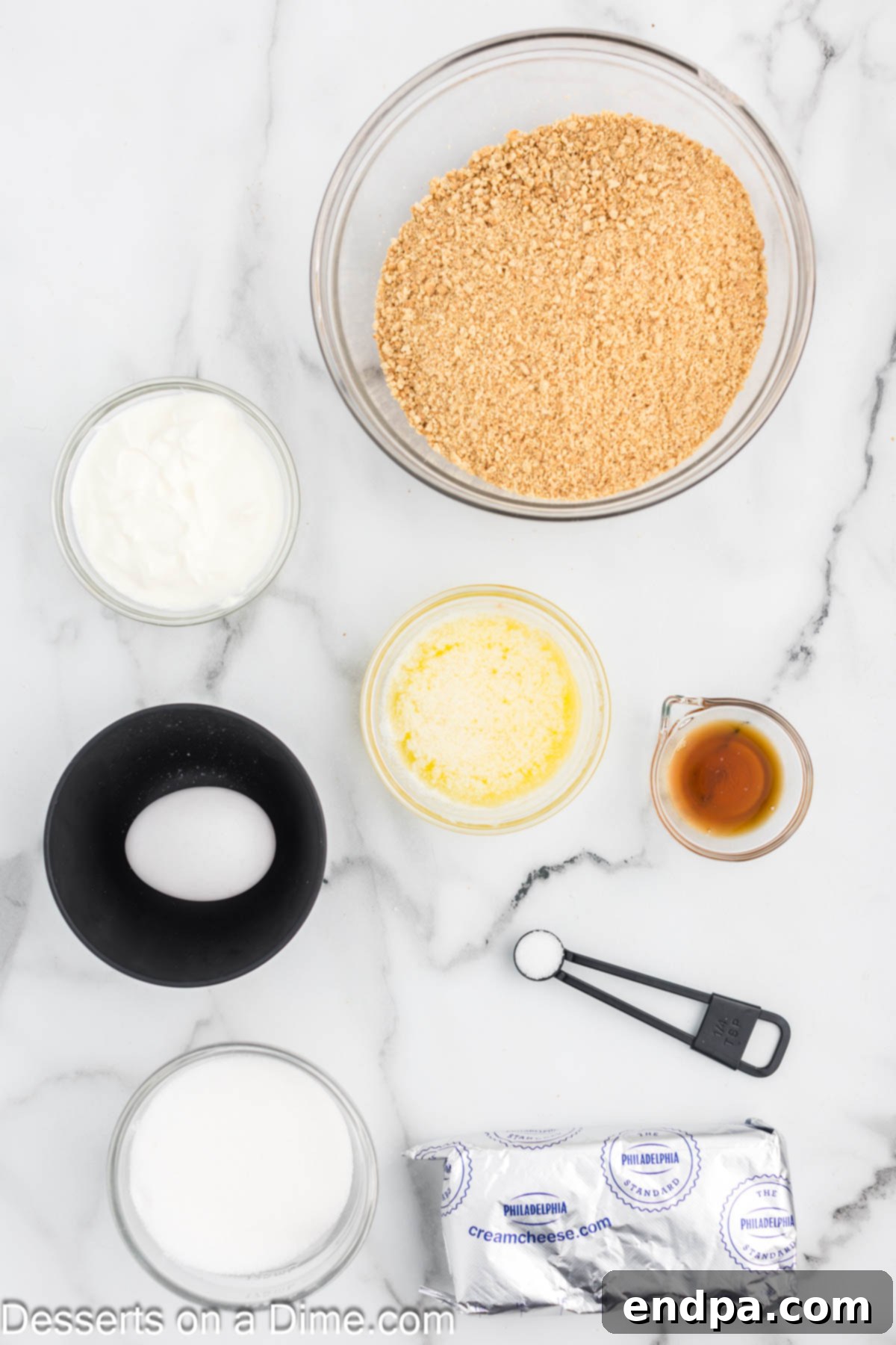 Ingredients for mini cheesecakes- graham cracker crust, sour cream. vanilla, cream cheese, milk, melted butter, laid out on a table.